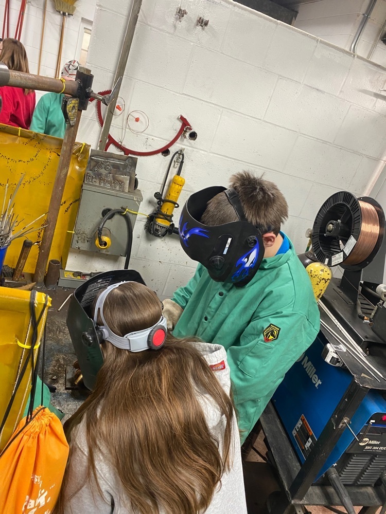 career center student helping 8th grader with welding practice